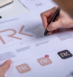 A designer sketches modifications on logo drafts featuring the initials 
