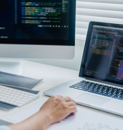 person coding on a laptop and a desktop screen