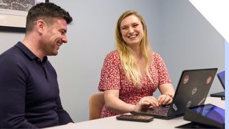 Two colleagues laughing and enjoying a productive meeting in the office with laptops on the desk.