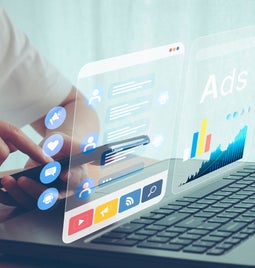 a woman tapping a smart phone with a laptop open in front of her and the word 