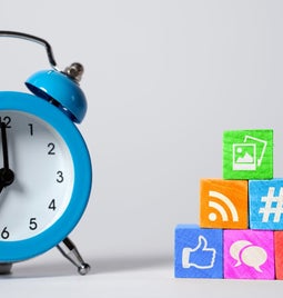 a blue alarm clock next to multicolored wooden blocks with social media icons on