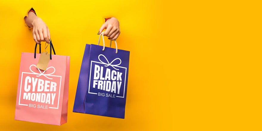 Hands popping out of a yellow backdrop holding Black Friday Cyber Monday branded shopping bags