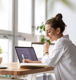 Woman working at her laptop on a desk by a large window