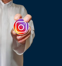 Person in white shirt holding up a sticker of the Facebook logo and the Instagram logo in each hand