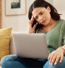 Woman looking puzzled with her hand against her head as she stares at a laptop