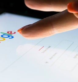 A closeup of a finger tapping the Google logo on its homepage