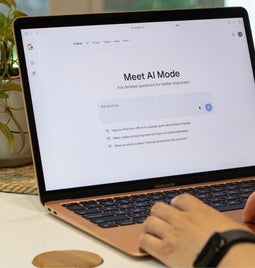 Hands typing on a laptop with the Google AI Mode landing page on screen