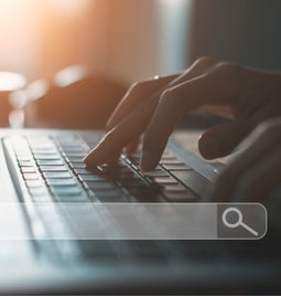 Hands typing at a laptop with a floating image of a search bar on top
