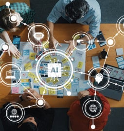Team sitting and working around a table with icons floating above showing AI icons and other digital tools