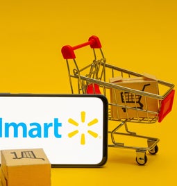 walmart logo on horizontal phone propped up by a small shopping cart with boxes in it