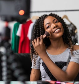 Person filming themself doing their makeup and smiling at the camera
