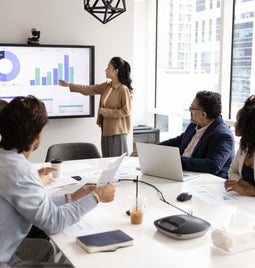 Colleagues sitting around a table watching a manager present on screen