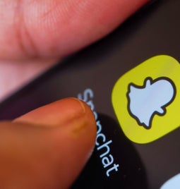 Close up image of a thumb tapping the snapchat logo on a smartphone homepage