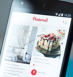 A smartphone displaying the Pinterest app, featuring holiday decor ideas and a dessert recipe, showcased on a colorful interface.
