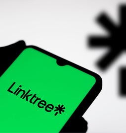 A hand holding a phone with the Linktree logo on screen