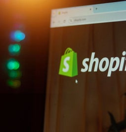 Close-up of a computer screen displaying the Shopify website logo with colorful lights in the background, hinting at a tech environment.