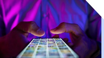 A person holding a smartphone illuminated by colorful lights, scrolling through a grid of images on the screen.