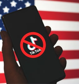 Hand holding phone with a banned TikTok logo, against a backdrop of the US flag