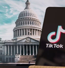 A phone with the TikTok logo on screen in front of a photo of the White House