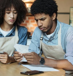 Two cafe workers looking concerned over paperwork and bills