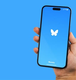 bluesky logo on phone being held in front of a blue background