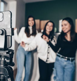 three ladies standing in front of a phone on a tripod