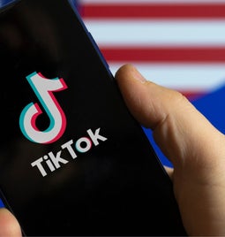 Phone with TikTok logo on the screen being held in front of an American flag