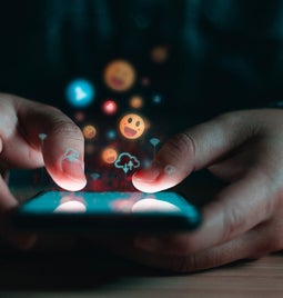 person typing on phone with emojis popping out the screen